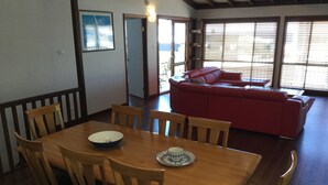 Un coin repas avec une table et des chaises en bois, un canapé rouge en arrière-plan et une vue par les fenêtres.