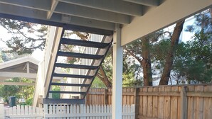 Un espace extérieur abrité doté d’une terrasse en bois, d’une clôture blanche en piquets et d’un pot de fleurs.