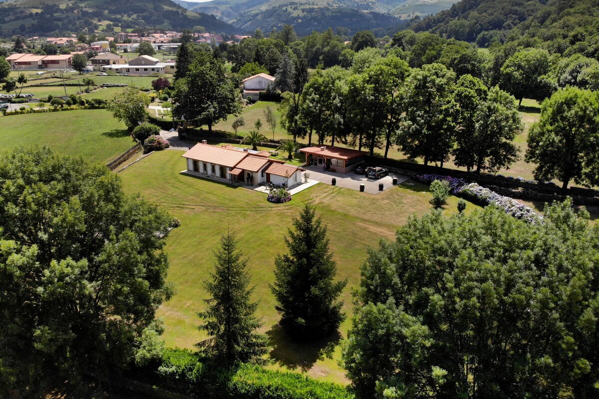 Uma casa térrea grande com telhado vermelho, cercada por um gramado bem cuidado e árvores.