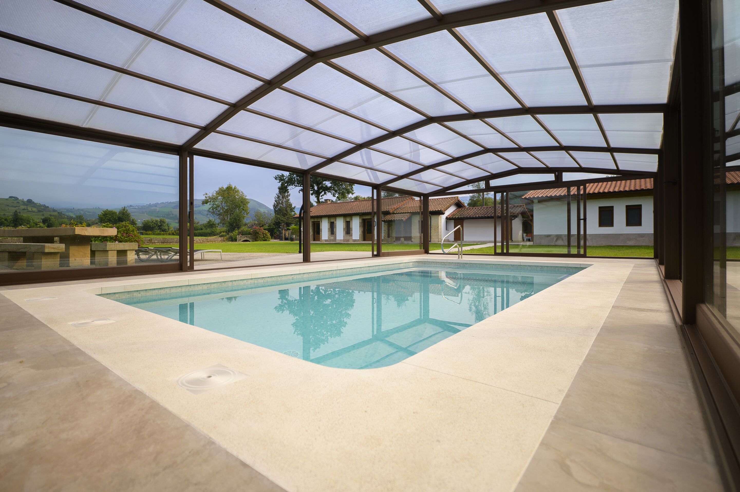 A covered swimming pool with a view of a house and landscape.