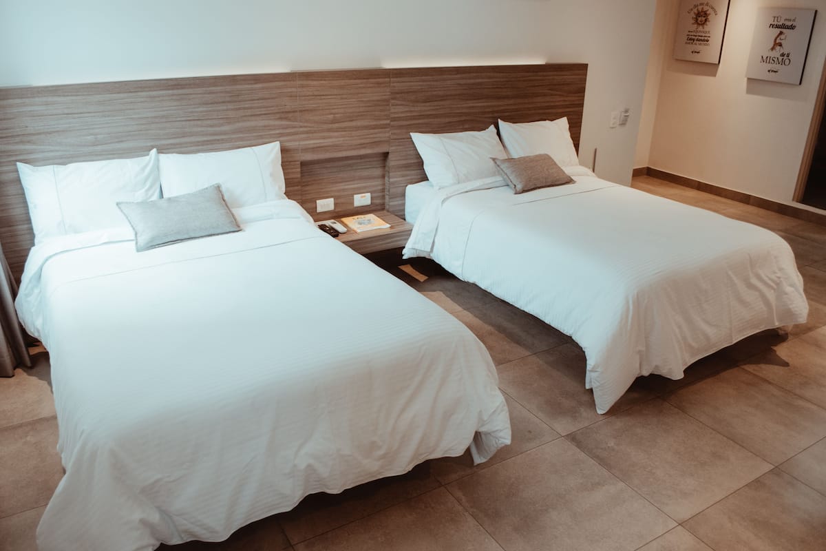 Two single beds with wooden headboards, white bedding, and a small bedside table with a book and remote control.