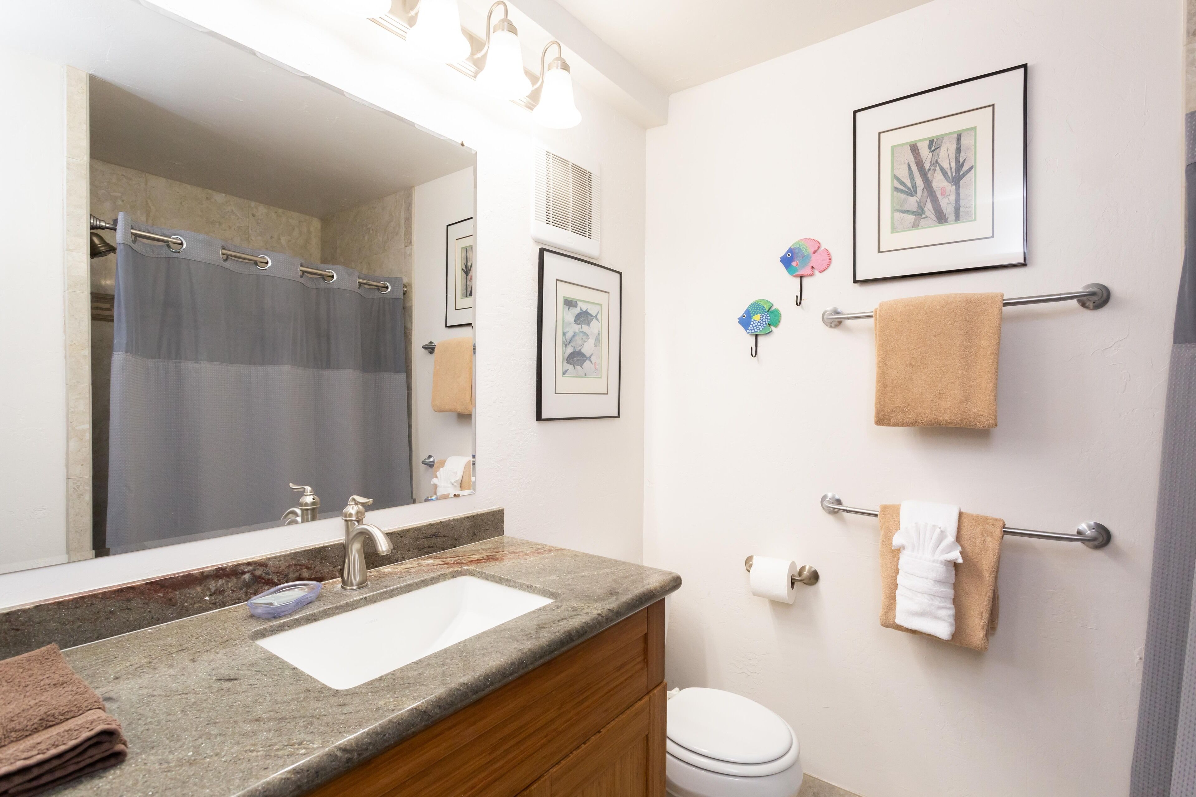 A bathroom with a granite countertop sink, a mirror, a toilet, and framed pictures on the wall.