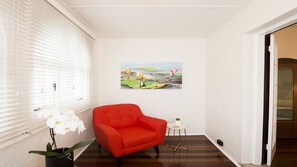 Una habitación con un sillón rojo, una pequeña mesa blanca, un cuadro de nenúfares y una orquídea en maceta.