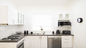 Una cocina moderna con armarios blancos, estufa a gas, lavavajillas, microondas y un fregadero.