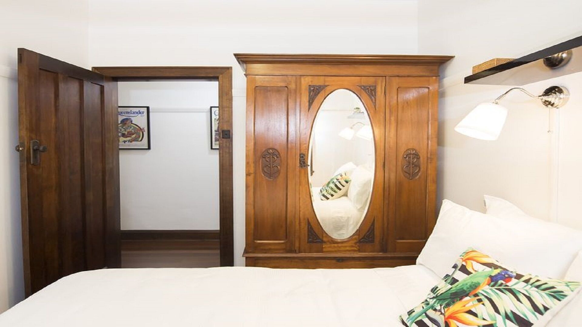 A bedroom with a large wooden wardrobe, a bed with white bedding, and a wall-mounted lamp.