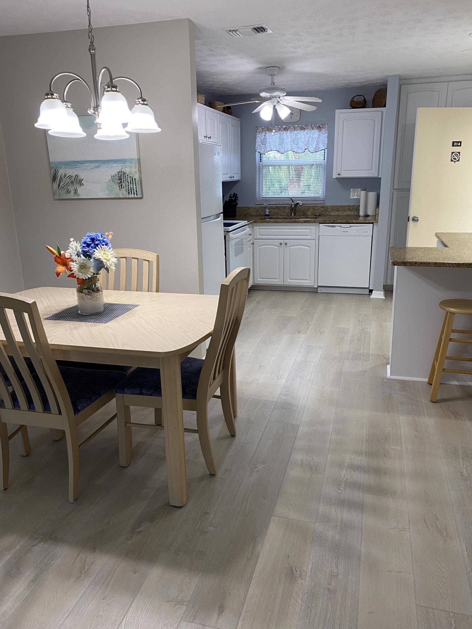 A dining area with a wooden table and chairs, a vase of flowers, and a kitchen in the background.