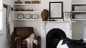 A room with a brown leather armchair, a fireplace, shelves with baskets and framed pictures, and a hanging towel.
