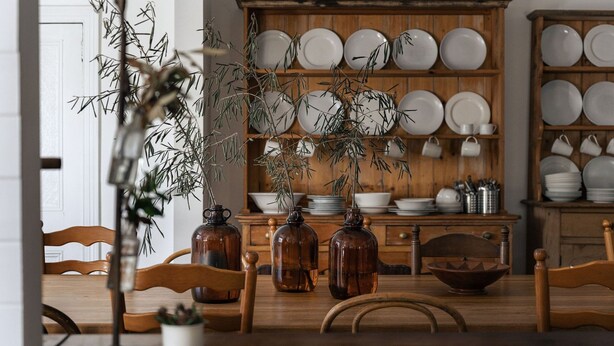 A dining area with wooden chairs, a table, and a backdrop of a wooden cabinet with plates and bowls. - Piccadilly House Daylesford ~ Walk to main street! (Daylesford)