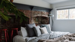 Een slaapkamer met een haard van baksteen, een bed met kussens, een rode kruk en een vloerlamp.