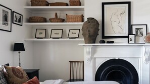A room with a fireplace, shelves with baskets and framed pictures, a lamp, and a bed with pillows.