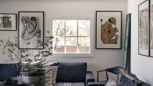 A living room with a sofa, a window, and abstract art on the walls. - Piccadilly House Daylesford ~ Walk to main street! (Daylesford)