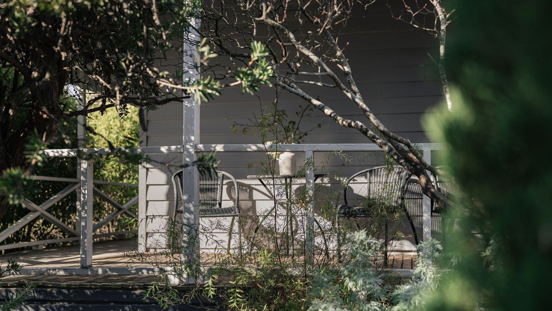 A garden area with a wooden pergola, a white chair, and a white wall in the background.