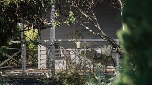 A garden area with a wooden pergola, a white chair, and a white wall in the background.