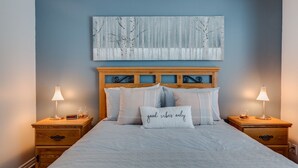A neatly made bed with a headboard, two bedside tables with lamps, and a wall-mounted abstract painting. - Condo Magog entre Ville et Nature (Magog)