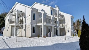 A multi-story residential building with balconies, a covered front porch, and a snow-covered ground. - Condo Magog entre Ville et Nature (Magog)