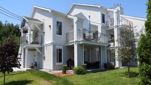 A two-story house with a covered porch and a small garden area. - Condo Magog entre Ville et Nature (Magog)