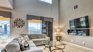 Ein modernes Wohnzimmer mit einem Ecksofa, einem Glastisch, einem Flachbildfernseher und einem Bücherregal.