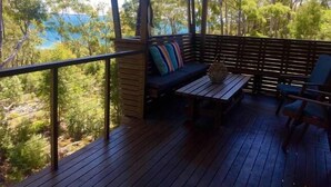 A covered outdoor seating area with a wooden deck, a bench with cushions, and a table.