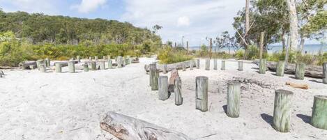 A sandy beach with wooden posts and a forested hill in the background.