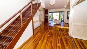A spacious hallway with a wooden floor, a staircase, and a view of a living area with a sofa and a coffee table.