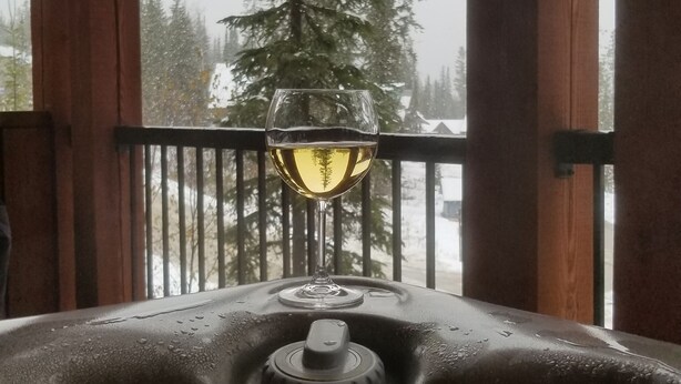 A wooden cabin with a balcony, a glass of white wine, and a snowy landscape with trees. - Slope Side  Luxury Open Beam Townhome Private Hot Tub - True - Ski-in-out (Golden)