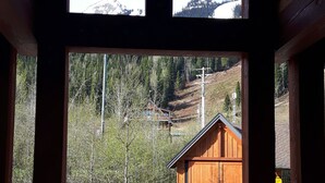 A wooden cabin with a stone foundation, a clear view of a mountain, and a paved driveway leading to the entrance. - Slope Side  Luxury Open Beam Townhome Private Hot Tub - True - Ski-in-out (Golden)