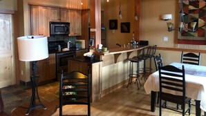 A spacious kitchen with wooden cabinets, a central island with bar stools, and a dining area with a table and chairs. - Slope Side  Luxury Open Beam Townhome Private Hot Tub - True - Ski-in-out (Golden)