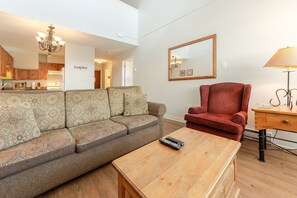 Een woonkamer met een bank, een rode fauteuil, een houten salontafel en een lamp.