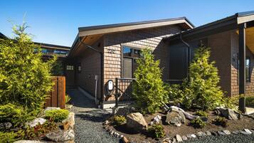 A modern building with a sloped roof, a wooden fence, and a gravel pathway with rocks and small trees.