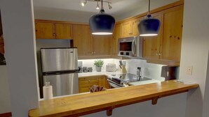 Een moderne keuken met houten kastjes, roestvrijstalen apparatuur en hangende lampen.