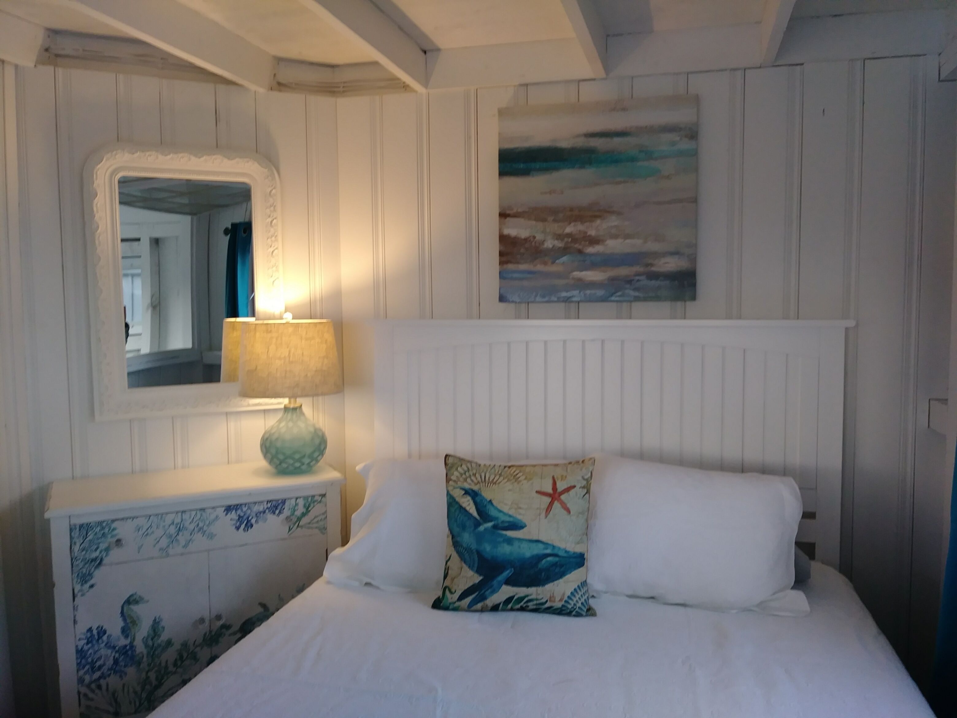 Une chambre à coucher avec un lit, une table de chevet avec une lampe, une commode à motifs floraux, un miroir et un tableau accroché au mur.