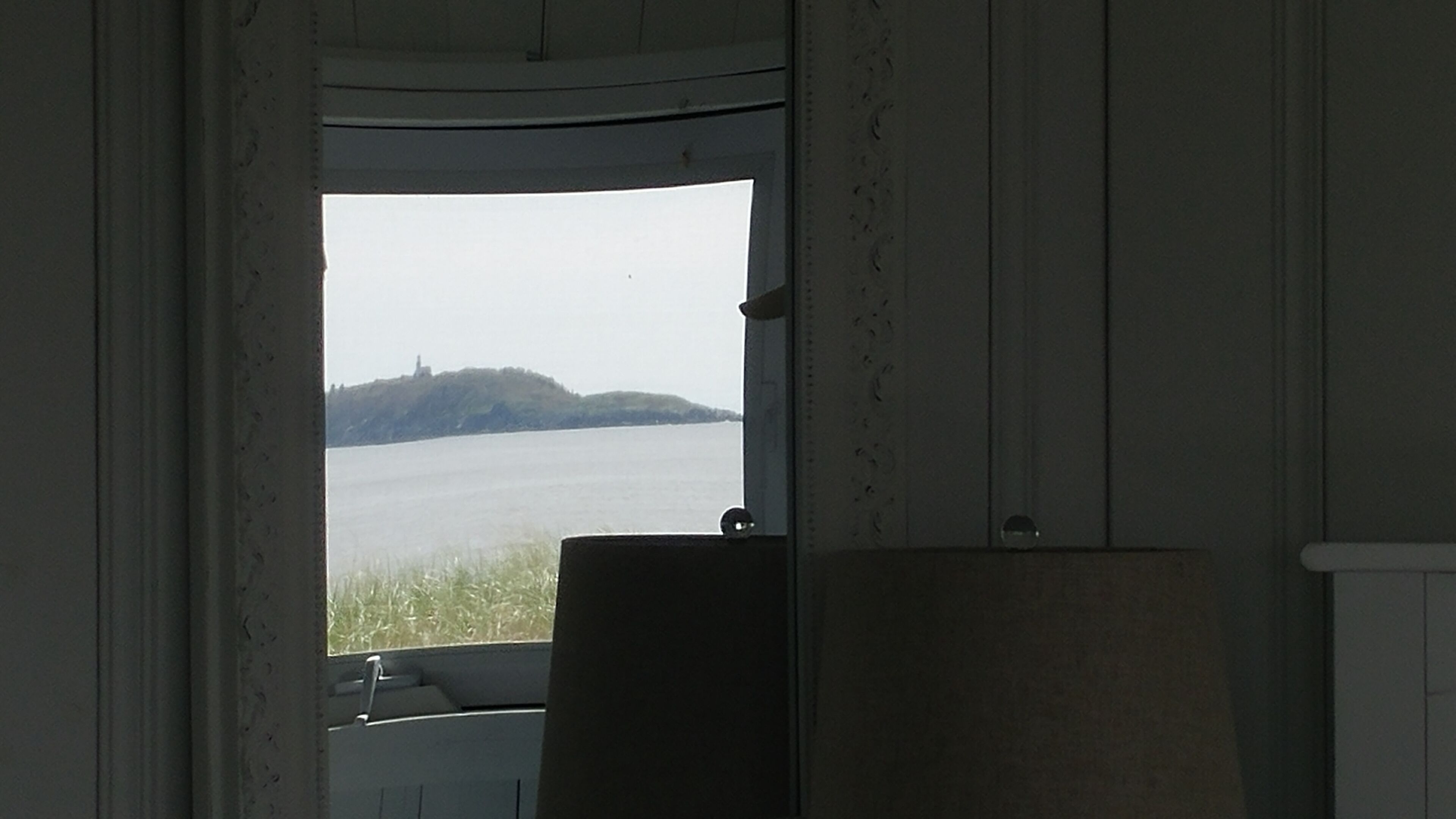 Una habitación con ventana que da a un cuerpo de agua y una colina distante.