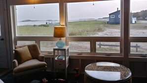 Una habitación con un ventanal grande, una silla, una lámpara y una mesa.