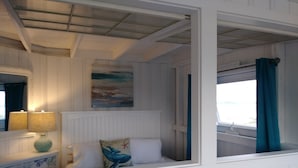Una habitación con una cama, una mesita de noche con lámpara, un cuadro en la pared y una ventana con cortinas.