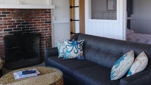 Una sala de estar acogedora con chimenea de ladrillo, un sofá azul oscuro con cojines estampados y una mesa de centro redonda hecha de fibras naturales.
