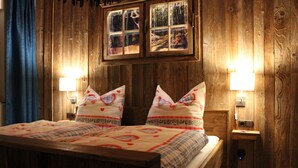 Ein Zimmer mit Holzwänden, einem Bett, zwei Wandleuchten und einem Fenster mit vielen Glasscheiben.