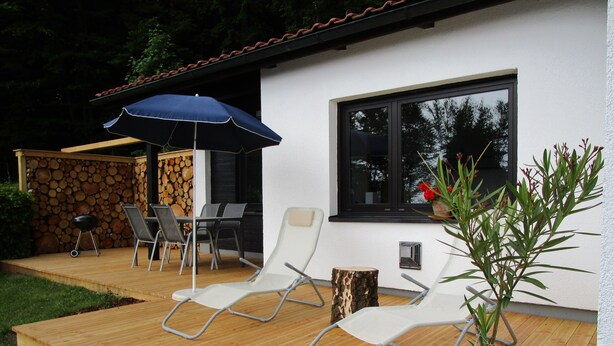Eine Holzterrasse mit zwei Liegestühlen, einem Tisch, einem Grill und einem Blumentopf.