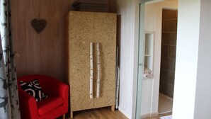 Ein Zimmer mit einem Holzschrank, einem roten Sessel mit gemustertem Kissen und einer herzförmigen Dekoration an der Wand.