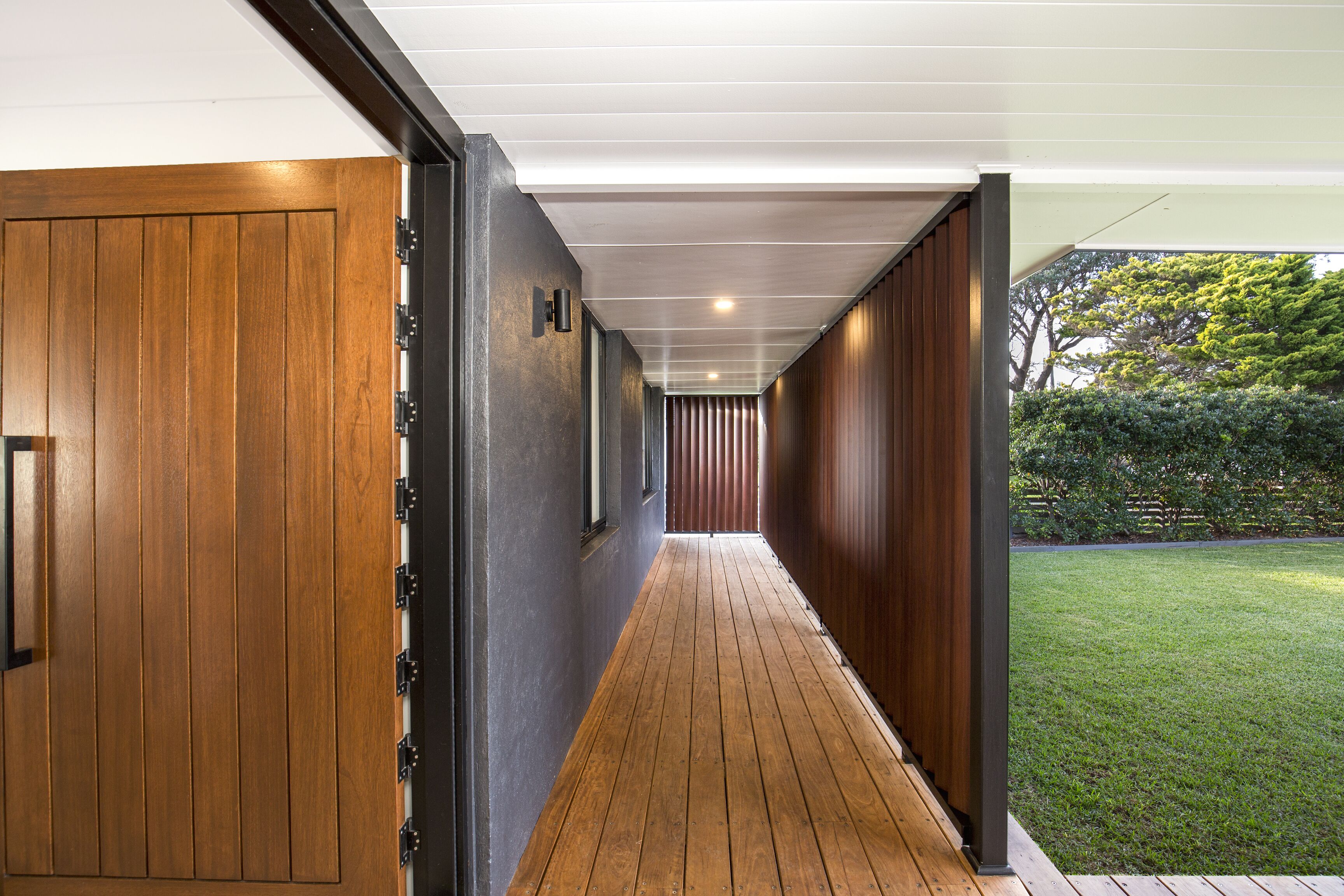 A corridor with wooden flooring and walls, leading to a garden area.