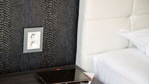 A neatly made bed with white linens, a dark wooden nightstand with a tablet and a framed picture, and a textured wall behind.