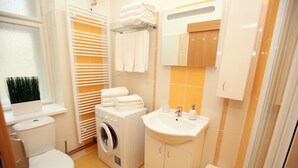A compact bathroom with a toilet, washing machine, sink, and towel rack.
