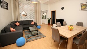 Ein modernes Wohnzimmer mit einer Eckcouch, einem Glastisch und einem Esstisch mit Stühlen.