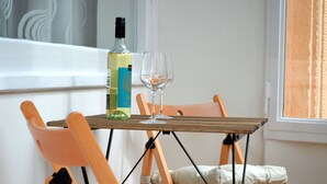 Ein kleiner Tisch mit einer Flasche und einem Glas, zwei orangefarbene Stühle und ein Fenster mit Vorhängen.