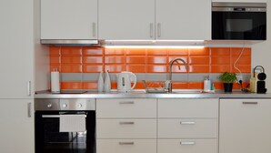 A modern kitchen with white cabinets, an orange backsplash, a stainless steel oven, and a built-in microwave.