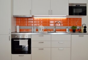 A modern kitchen with white cabinets, a stainless steel oven, a kettle, and a sink.