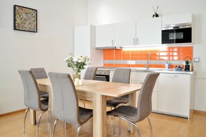 A modern kitchen with white cabinets, an orange backsplash, and a dining area with a wooden table and grey chairs.