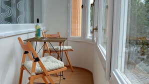 Ein Eckzimmer mit Holztisch und zwei Stühlen, einer Weinflasche und einem Fenster mit Blick auf Grünflächen.