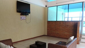 A room with a television mounted on the wall, a brick wall, and a large window. - Apartamento confortable (Bogotá)