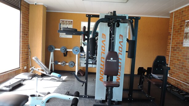 Et fitnesscenter med forskellig træningsudstyr, herunder en squat-stativ, håndvægte og en bænk.