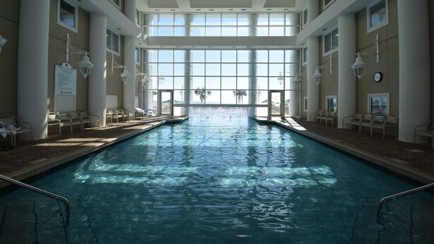 Une piscine intérieure avec des parois en verre transparent, de nombreuses fenêtres et des rangées de chaises le long des côtés.